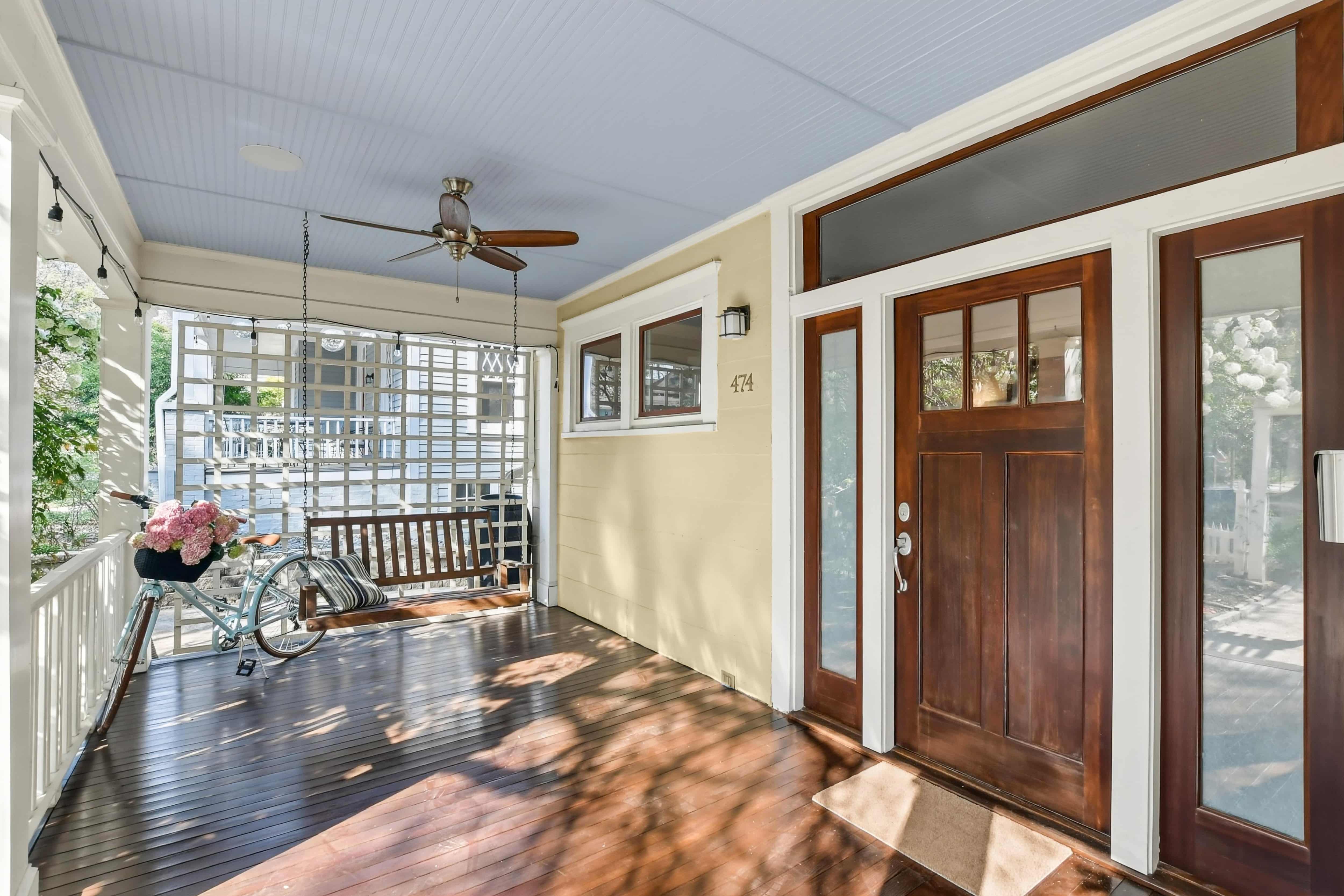 Craftsman-style front porch with a wooden swing, ceiling fan, and stained wood entry door with sidelights